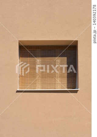 Window with a bamboo roller blind on a beige facade Window with a bamboo roller blind on a beige facade 140392178
