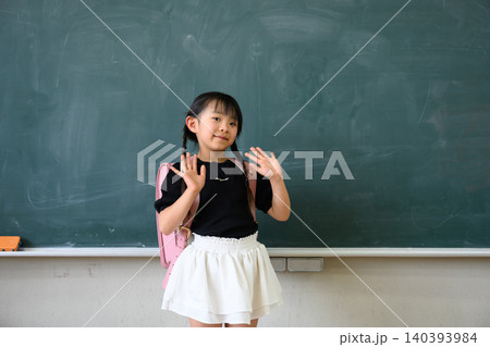 教室の黒板の前でランドセルを背負い両手を広げて笑顔を見せる小学1年生の女の子 140393984