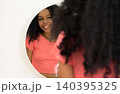 Beautiful dark skinned smiling girl in orange t-shirt looking at mirror admiring herself at home 140395325