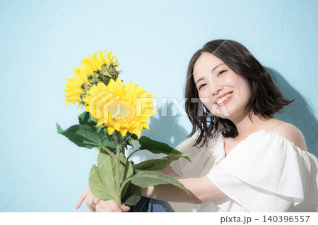 水色背景でひまわり(向日葵)の花束を持って笑顔の女性 爽やかな真夏のイメージ 水色背景でひまわり(向日葵)の花束を持って笑顔の女性 爽やかな真夏のイメージ 140396557