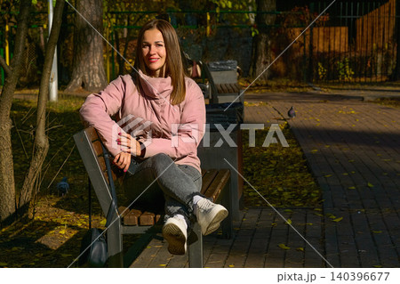 Charming smiling young woman in good mood sitting on bench in park Charming smiling young woman in good mood sitting on bench in park 140396677