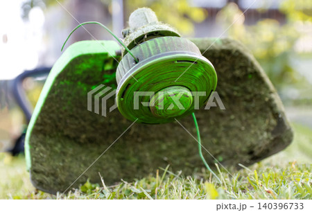 String trimmer head close up on green grass lawn. Ground level portrait of grass cutter machine with nylon line, garden weed eater tool, lawn mowing and backyard maintenance concept 140396733
