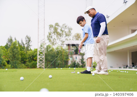 Golf instructor teaching young student to putt at practice green Golf instructor teaching young student to putt at practice green 140397406