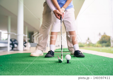 Professional coach guiding student for golf swing on green mat Professional coach guiding student for golf swing on green mat 140397411