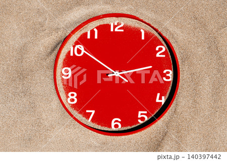 a red clock is nearly buried beneath fine sand a red clock is nearly buried beneath fine sand 140397442