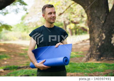 Man holding blue yoga mat in park for outdoor workout 140397491