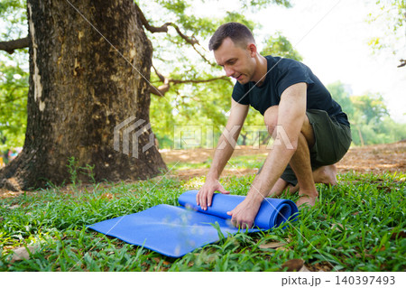 Fit man preparing exercise mat for outdoor yoga in the park Fit man preparing exercise mat for outdoor yoga in the park 140397493