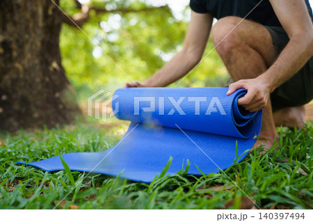 Fit man preparing exercise mat for outdoor yoga in the park Fit man preparing exercise mat for outdoor yoga in the park 140397494