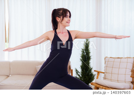 Woman practicing warrior ii yoga pose in bright living room Woman practicing warrior ii yoga pose in bright living room 140397603