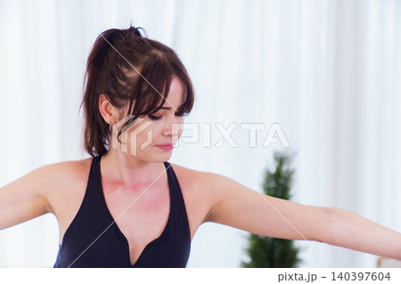 Woman practicing warrior ii yoga pose in bright living room Woman practicing warrior ii yoga pose in bright living room 140397604