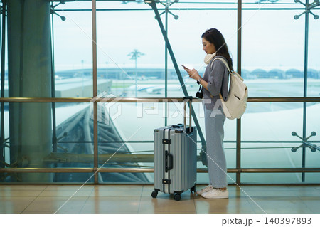 Asian woman waiting for boarding with luggage at airport departure gate Asian woman waiting for boarding with luggage at airport departure gate 140397893