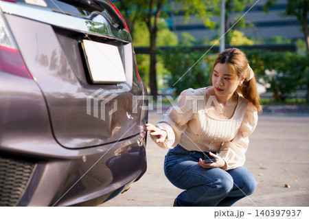 Woman inspecting damaged car bumper after minor accident Woman inspecting damaged car bumper after minor accident 140397937