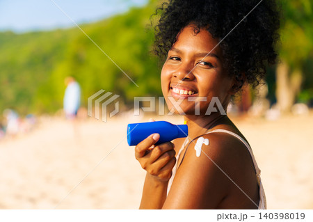 Woman applying sunscreen lotion on shoulder at the beach Woman applying sunscreen lotion on shoulder at the beach 140398019
