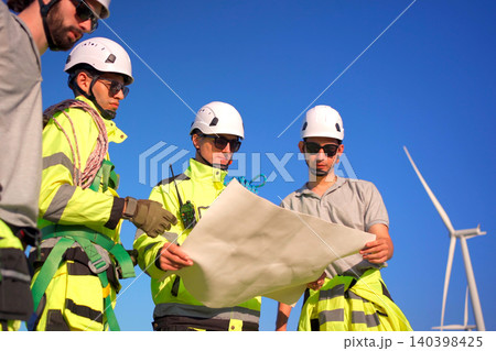 Engineers discussing a blueprint plan at a wind turbine farm Engineers discussing a blueprint plan at a wind turbine farm 140398425