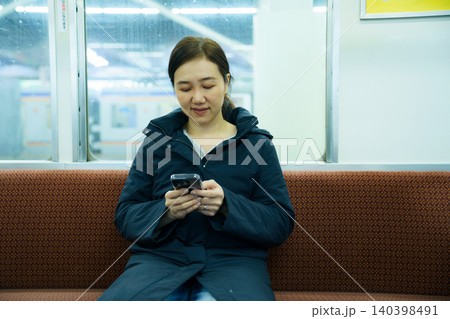 Asian woman using smartphone while traveling on a train Asian woman using smartphone while traveling on a train 140398491