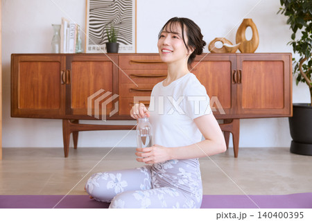 自宅でヨガの休憩中に水を飲む笑顔の若い女性 自宅でヨガの休憩中に水を飲む笑顔の若い女性 140400395