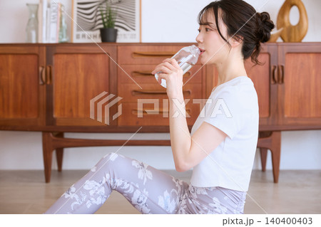 自宅でヨガの後に水を飲むスポーツウェア姿の若い女性 140400403