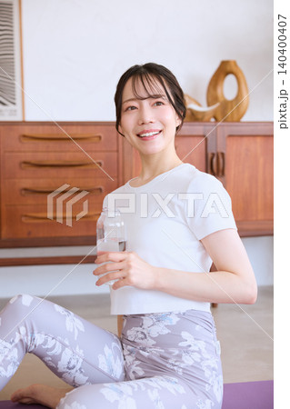自宅でヨガの後に水分補給する笑顔の若い女性 140400407