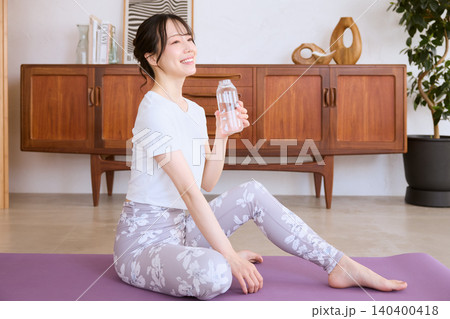 自宅でヨガの休憩中に水を飲む笑顔の若い女性 140400418
