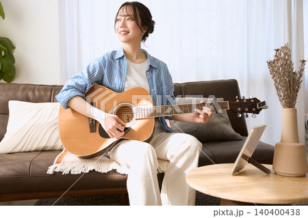 リビングのソファでアコースティックギターを弾く笑顔の若い女性 リビングのソファでアコースティックギターを弾く笑顔の若い女性 140400438