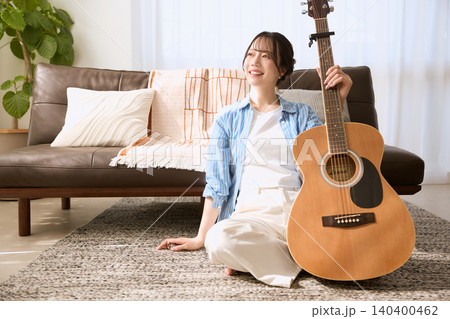 リビングでアコースティックギターを持つ笑顔の若い女性 リビングでアコースティックギターを持つ笑顔の若い女性 140400462