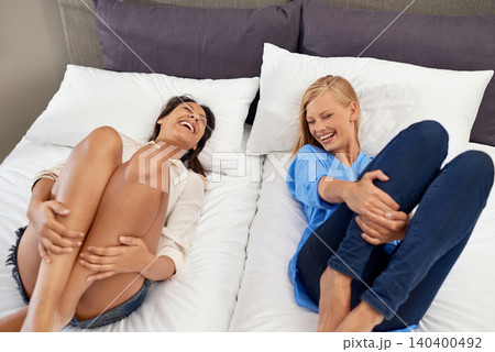 Women, friends and laughing on bed for relax vacation in hotel for bonding connection, humor or accommodation. Female people, funny and joke on happy getaway in London for resting, comedy or together 140400492