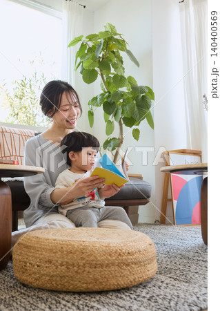 リビングでソファに座り子供に絵本を読み聞かせる母親 リビングでソファに座り子供に絵本を読み聞かせる母親 140400569