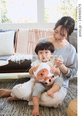 リビングで子どもの歯磨きをする母親とぬいぐるみを抱く幼児 リビングで子どもの歯磨きをする母親とぬいぐるみを抱く幼児 140400579