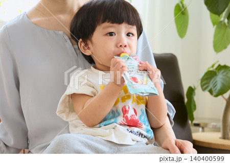 母親の膝の上でフルーツピューレのパウチを飲む幼児 母親の膝の上でフルーツピューレのパウチを飲む幼児 140400599