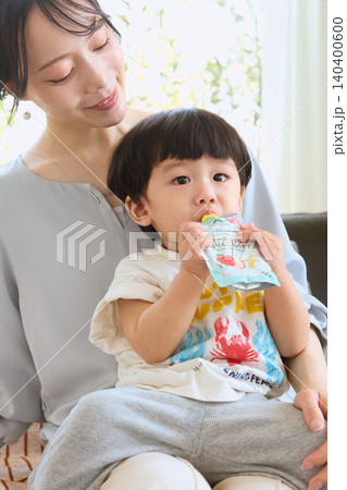 母親の膝の上でパウチ飲料を飲む幼児 母親の膝の上でパウチ飲料を飲む幼児 140400600
