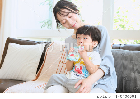 ソファでベビーフードのパウチを食べる幼児と見守る母親 ソファでベビーフードのパウチを食べる幼児と見守る母親 140400601