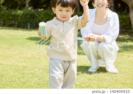 芝生の公園でおもちゃを持って遊ぶ男の子と見守る母親 140400910