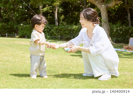 公園の芝生で母親と手をつないで遊ぶ幼い男の子 140400914