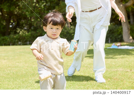 公園の芝生で積み木を持って走る幼児と追いかける親 140400917