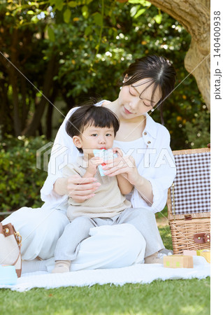 公園でピクニックを楽しむ母親と飲み物を飲む幼児 公園でピクニックを楽しむ母親と飲み物を飲む幼児 140400938