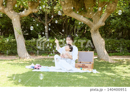 公園の木陰でシャボン玉を楽しむ母親と子供のピクニック 公園の木陰でシャボン玉を楽しむ母親と子供のピクニック 140400951