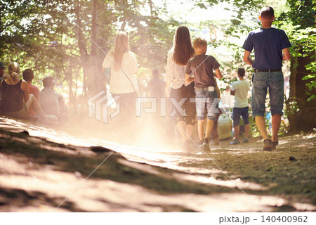 Festival, party and family walking in forest outdoor together for event, celebration or social gathering. Mother, father and children in nature, park or woods for summer entertainment from back 140400962