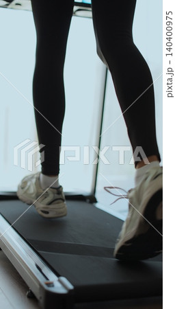 Vertical video. Closeup of a woman legs running on a treadmill at home. Back view of legs having workout on treadmill. 140400975