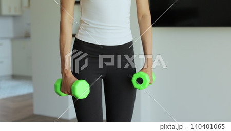 Close up young sports girl in leggings does exercises with dumbbells. Healthy lifestyle. Woman goes in for sports outdoor at home. Close up young sports girl in leggings does exercises with dumbbells. Healthy lifestyle. Woman goes in for sports outdoor at home. 140401065