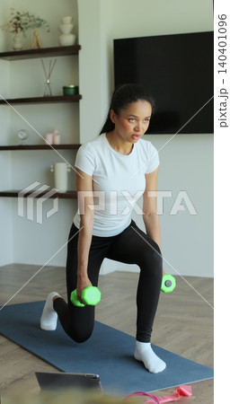Vertical video. Athletic young woman in sportswear training at home, performing squats with dumbbells in her hands, enjoying a healthy lifestyle. Athletic woman doing training. Vertical video. Athletic young woman in sportswear training at home, performing squats with dumbbells in her hands, enjoying a healthy lifestyle. Athletic woman doing training. 140401096