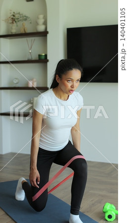Vertical video. Attractive woman trains her buttocks and leg muscles on a blue carpet at home. Sports female doing training. Vertical video. Attractive woman trains her buttocks and leg muscles on a blue carpet at home. Sports female doing training. 140401105