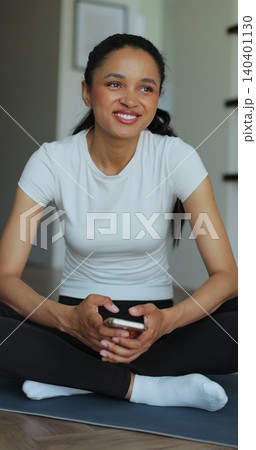 Vertical Video. Portrait of a sporty woman resting at home after training and using her smartphone. Beautiful healthy sportive girl athlete resting after intense hard training. Vertical Video. Portrait of a sporty woman resting at home after training and using her smartphone. Beautiful healthy sportive girl athlete resting after intense hard training. 140401130