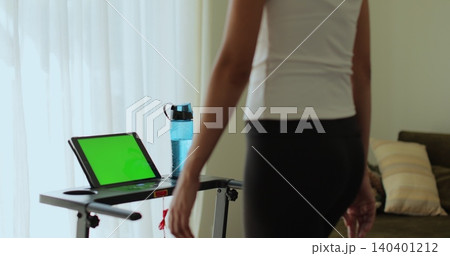 Back view. Fitness, girl and walking on treadmill in home for cardio exercise, wellness challenge and burning calories. Tablet with green screen, workout video. Back view. Fitness, girl and walking on treadmill in home for cardio exercise, wellness challenge and burning calories. Tablet with green screen, workout video. 140401212