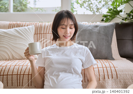 リビングのソファでコーヒーカップを持ちくつろぐ若い妊婦 リビングのソファでコーヒーカップを持ちくつろぐ若い妊婦 140401392