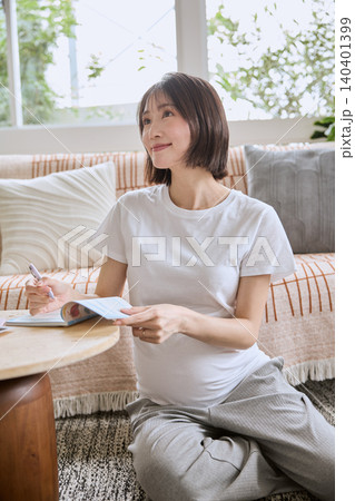 リビングのソファでくつろぎながら母子手帳を書く妊婦 140401399