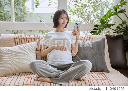 ソファに座りスマートフォンを見る妊婦 140401403