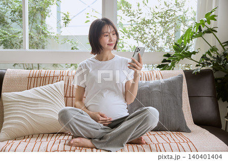 ソファに座りスマートフォンを見る妊婦 140401404