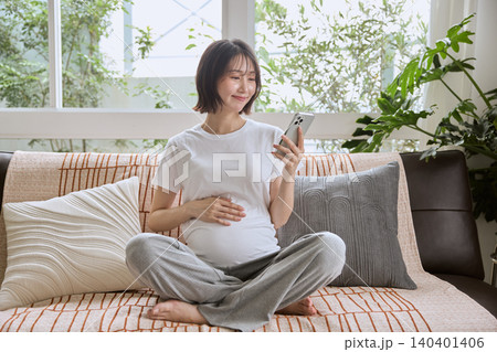 ソファに座りスマートフォンを見る笑顔の妊婦 ソファに座りスマートフォンを見る笑顔の妊婦 140401406