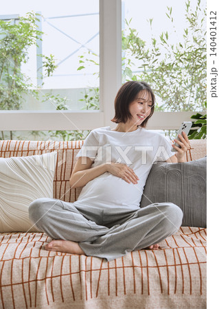 ソファでスマートフォンを見ながらくつろぐ妊婦 ソファでスマートフォンを見ながらくつろぐ妊婦 140401412