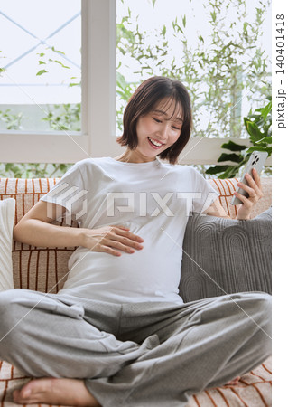 ソファでスマホを見ながら笑顔でくつろぐ妊婦 ソファでスマホを見ながら笑顔でくつろぐ妊婦 140401418